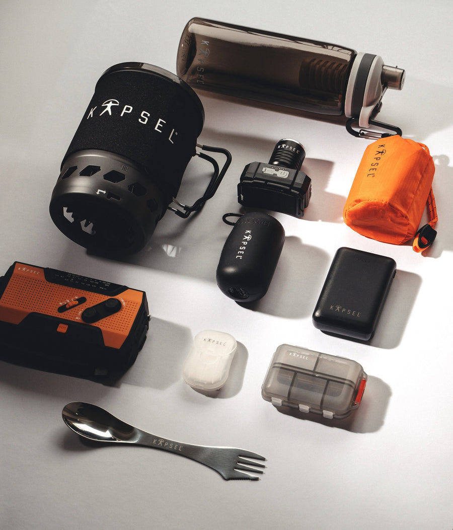 Delarna ur Kapsel Core utlagda på ett bord: kök, pannlampa, powerbank, filterflaska och bestick