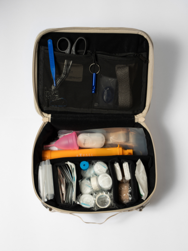 Open desert sand preparedness and emergency bag first aid kit with various items on a white background